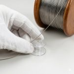 Gloved hand demonstrating the extreme fineness and flexibility of 0.05mm thin titanium wire from Beiyu Titanium