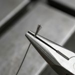 Close-up of ultra-thin titanium wire held by pliers, showcasing exceptional thinness and strength for aerospace and medical applications