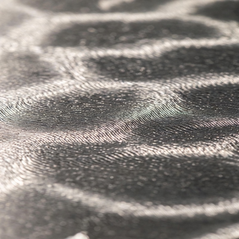 Close-up surface detail of precision titanium build plate showing optimized texture for strong powder adhesion in 3D printing