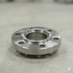 Titanium flange lying face up, showing the raised face and the bolt hole pattern