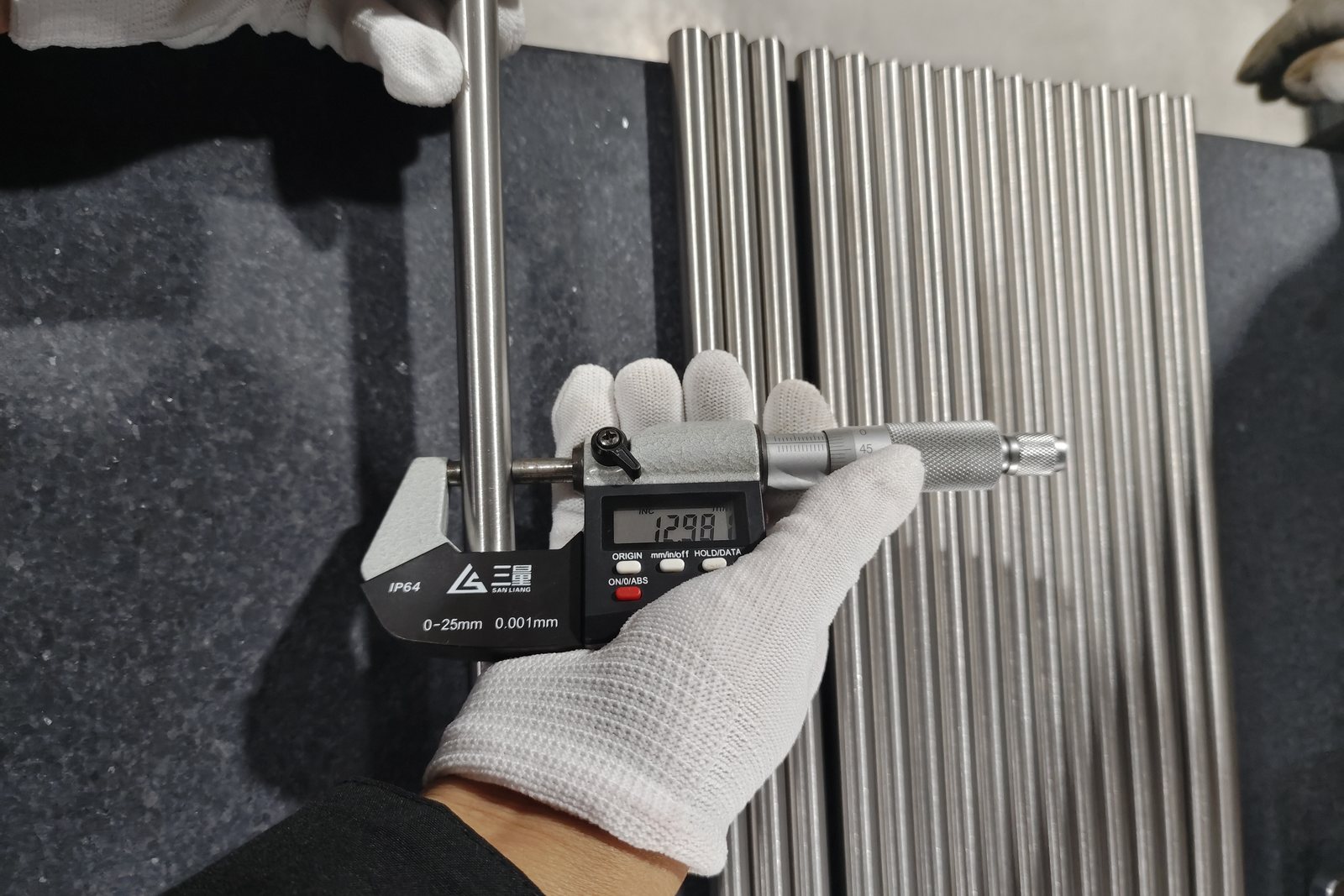 Digital micrometer reading titanium bar diameter on a granite surface plate