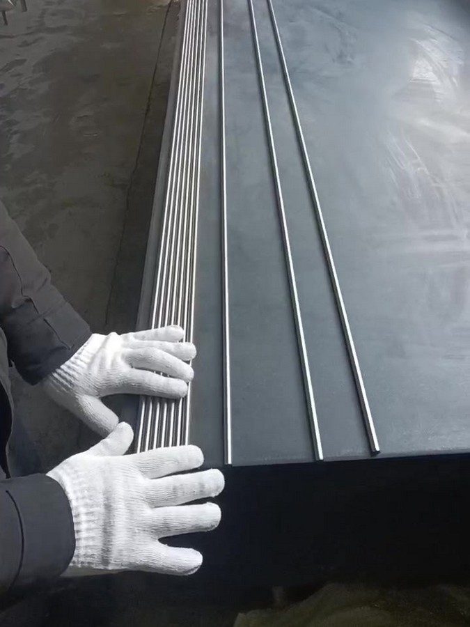 Operator checking titanium bar straightness against a surface plate